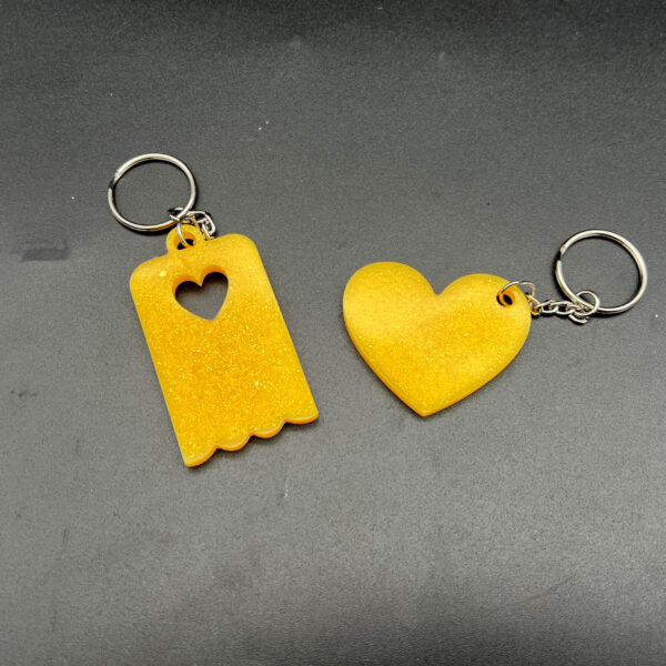 Two keychains made with yellow resin and glitter. On the left is a rectangular keychain with a scalloped bottom and a heart cut out at the top. On the right is a heart. Both have silver keychain hardware.
