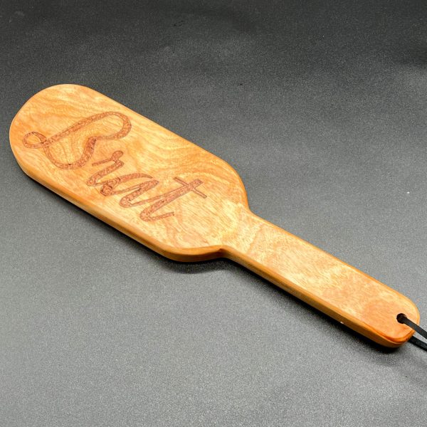 A 12 inch long wooden paddle with the word Brat burned into the center of the paddle area. The paddle is 7 inches long and is in an oval shape. The handle is 5 inches long, 1.25 inches wide, and straight with no curves.