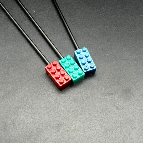 Close-up of building brick tips to show detail and color. Left to right: red, teal, and blue. Each one has 8 connector bumps and the tip is a rectangle shape