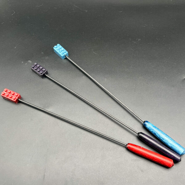 3 Diabolical Sticks with building bricks made with resin on the top and resin handles at the bottom. The rod is made of carbon fiber. The colors, from left to right, are red, purple, and blue.