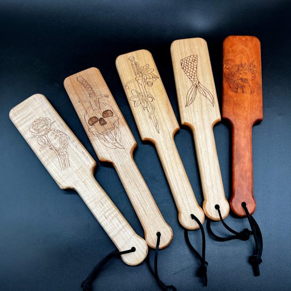 Current selection of Burn Baby Burn paddles available. Left to right: Rose and Skeleton in curly maple, Skull and Dagger in maple, Sword and Flowers in Maple, Mermaid tail in Maple, Unicorn in Cherry