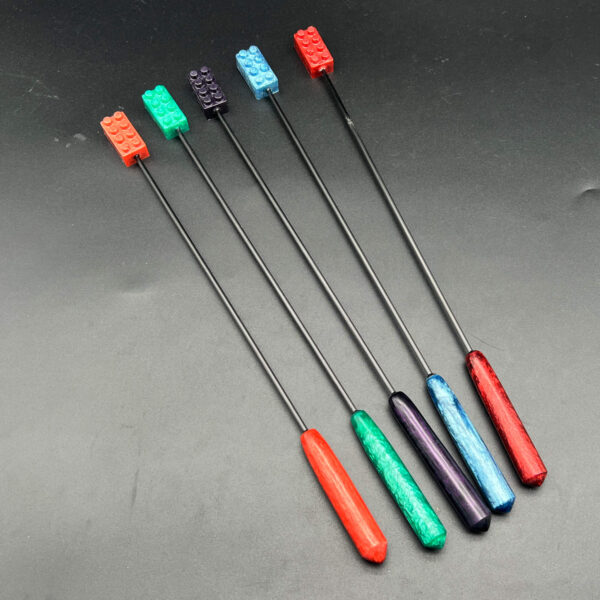 Five diabolical sticks with building brick tips. From left to right, the colors pictured are: rose gold, teal, purple, blue, and red