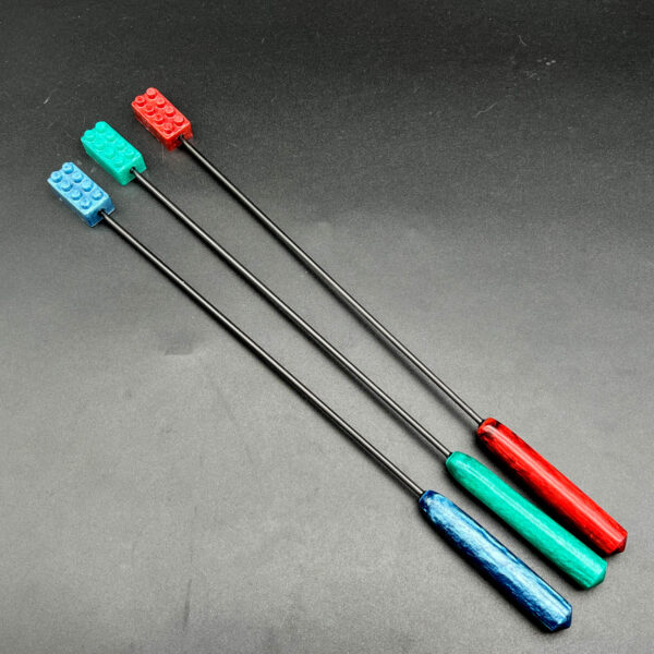 Three diabolical sticks with building brick tips made of resin. From left to right: blue, teal, and red