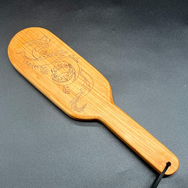 A 12 inch long wooden paddle with the side profile of a dragon burned into the center of the paddle area. The paddle is 7 inches long and is in an oval shape. The handle is 5 inches long, 1.25 inches wide, and straight with no curves.