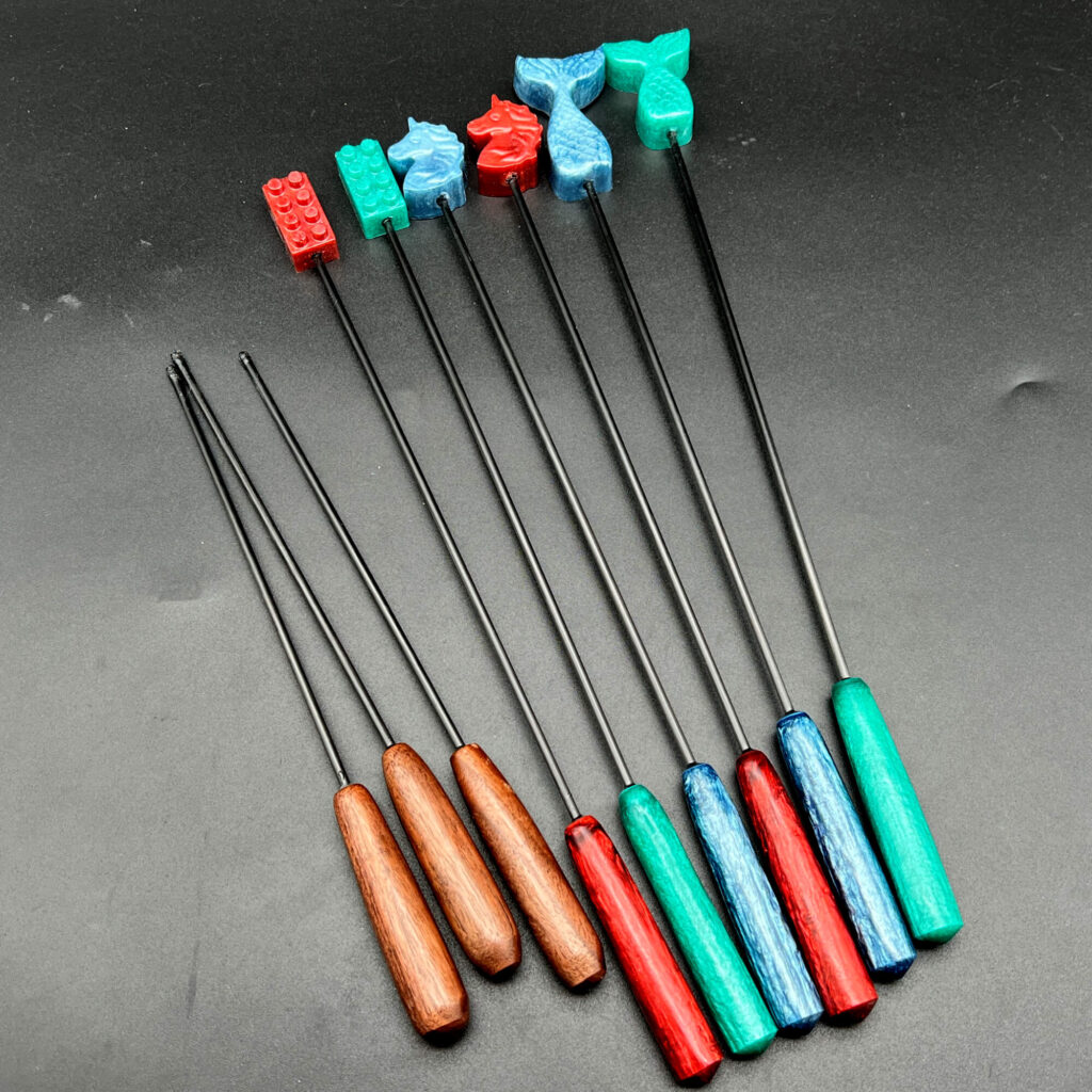 Three evil sticks -- rubber tipped carbon fiber rods with a wooden handle and an array of Diabolical sticks, carbon fiber rods with resin handles and resin shapes at the other end: building bricks, unicorn heads, and mermaid tails in an array of colors