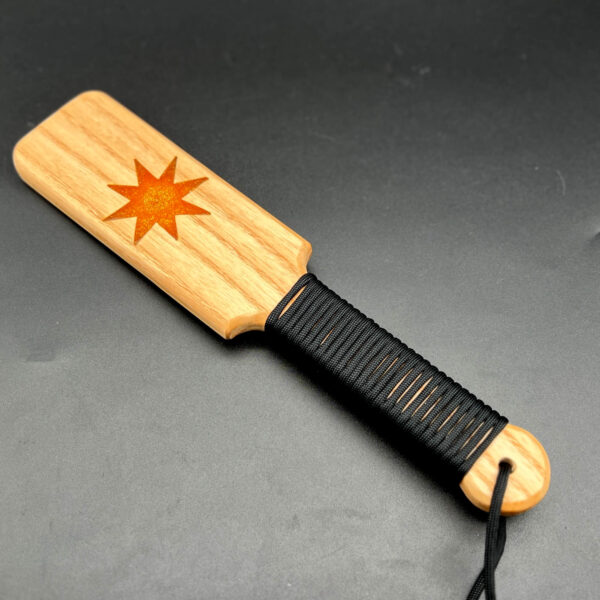Small wooden paddle made of Ash with golden resin 8-point star in the center and black paracord around the handle