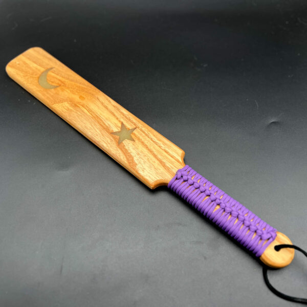 Large wooden paddle made of Ash with glow-in-the-dark resin crescent moon and star and purple paracord around the handle