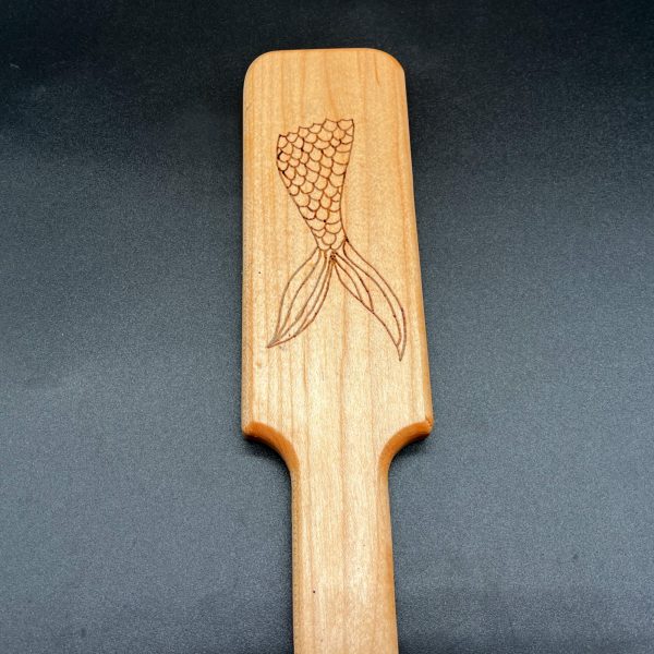 Close up view of a wood burned design in a wooden paddle: mermaid's tail