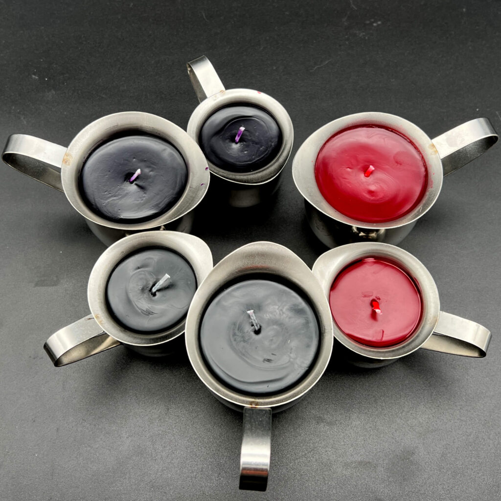 Group of small (3oz) and large (5oz) paraffin wax play candles. On the right, red candles. On the top left, purple, and on the bottom left, black. All candles are in silver containers with handles.