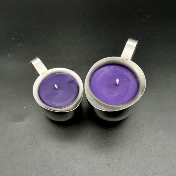 Overhead view of two purple soy wax play candles; small (3oz) on left and large (5oz) on right. The candles are in silver creamer containers with handles and have white wicks in the center.