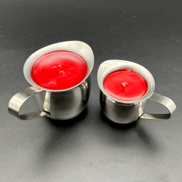 Two red paraffin wax play candles. On the left, the large (5oz) and on the right, the small (3oz). Both are in silver containers with handles.