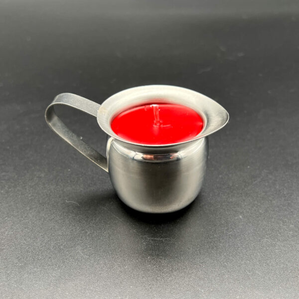Side view of single red paraffin wax play candle in silver container with handle