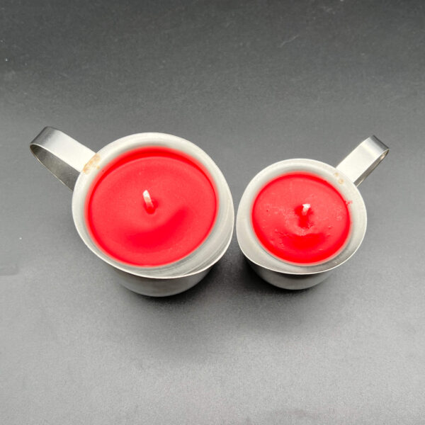 Overhead view of two red soy wax play candles. On the left, the large (5oz) and on the right the small (3oz). Both are in silver containers with handles.