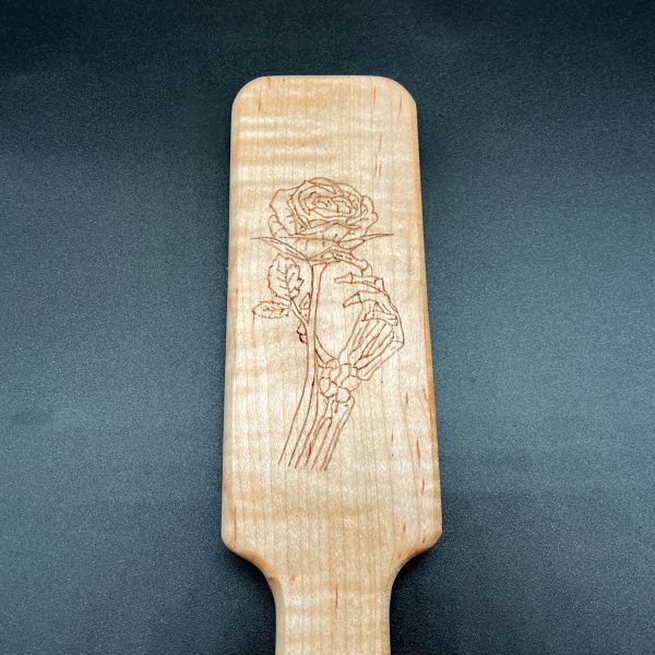 Close up view of the wood burned design on a wooden paddle - a skeletal hand holding a rose