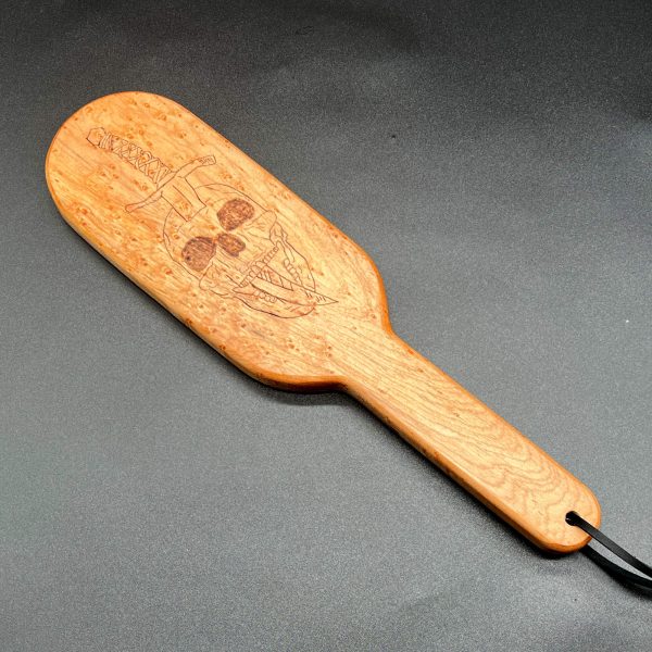 A 12 inch long wooden paddle with a skull with a dagger stabbed through the top of the head and coming out of the mouth burned into the center of the paddle area. The paddle is 7 inches long and is in an oval shape. The handle is 5 inches long, 1.25 inches wide, and straight with no curves.