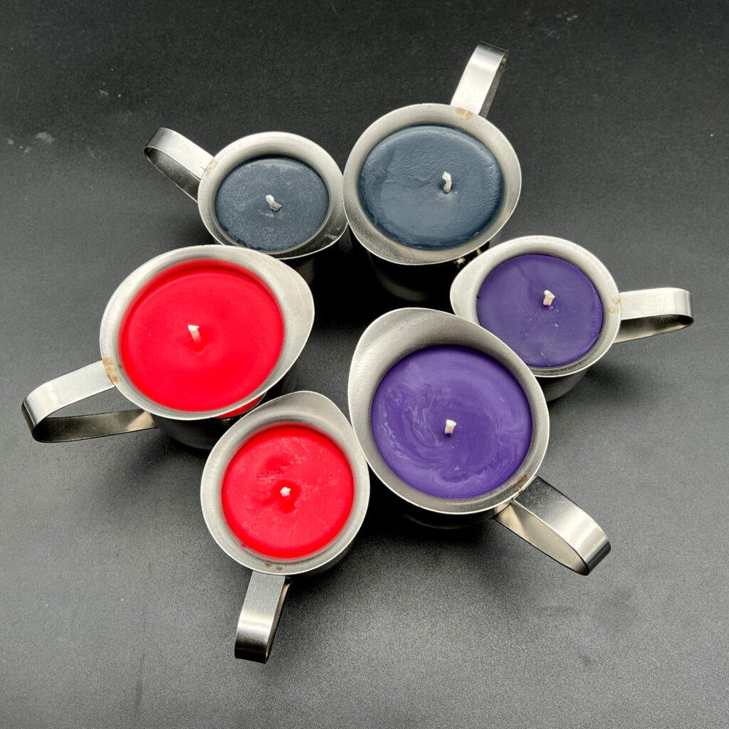 Group of soy candles. Top is black in large (5oz) and small (3oz). To the right is purple in small and large. To the left is red in small and large. All soy wax play candles are in silver containers with handles.