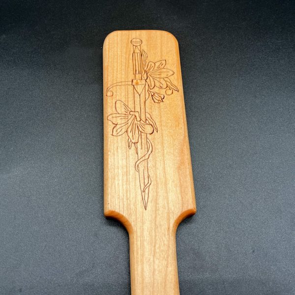 Close up view of the wood burned design in a wooden paddle: Sword with flowers winding around the length of it