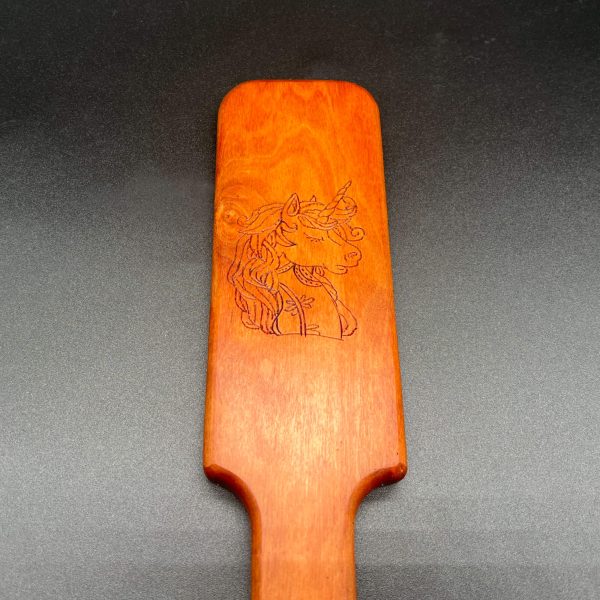 Close up view of a wood burned design in a wooden paddle: unicorn