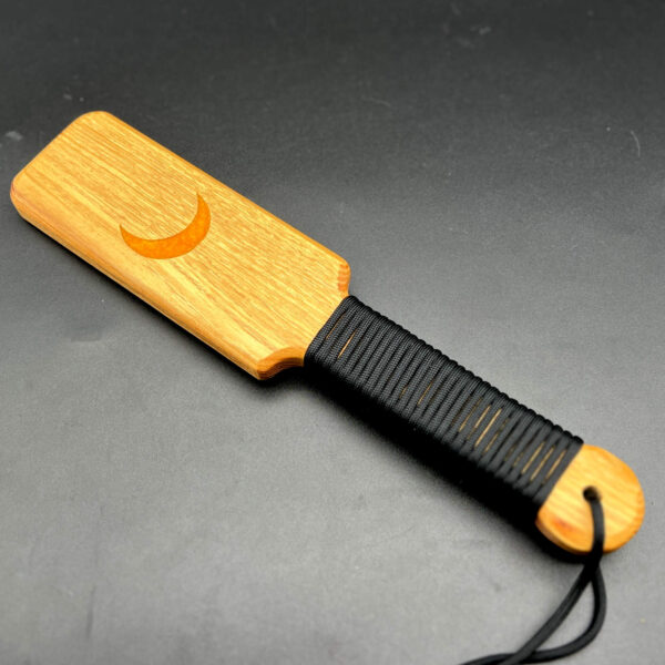 Small wooden paddle made of black locust with yellow resin crescent moon in the center and black paracord around the handle