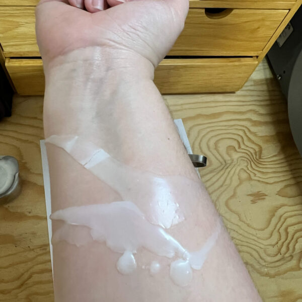 white/dye-free paraffin wax poured onto Kayla's forearm to show color. Kayla is a white woman and her skin is extremely pale. The white paraffin shows up but is not completely opaque on the first layer.
