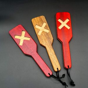 3 XOXO paddles in a row, each with the X facing up. Each paddle is made with two different woods - Maple is the center wood for each paddle. The outer woods, left to right: purpleheart, black limba, and paduak