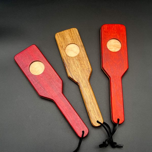 3 XOXO paddles in a row, each with the O facing up. Each paddle is made with two different woods - Maple is the center wood for each paddle. The outer woods, left to right: purpleheart, black limba, and paduak