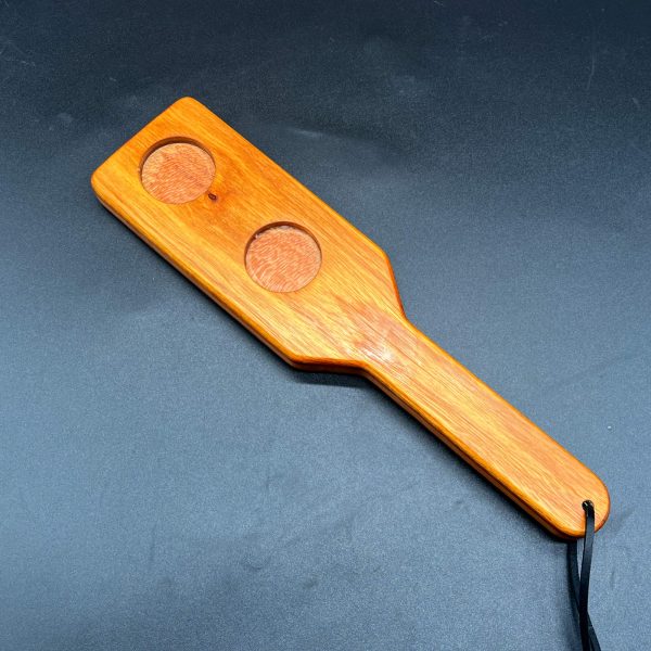 Wooden paddle made with Canarywood and Cherry. Three pieces of wood are glued together - Canarywood on the outside and Cherry in the center. Two holes have been cut through the Canarywood on one side and the Cherry is visible through the holes.