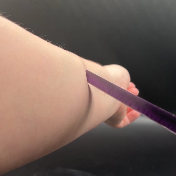 Close up of the tip of the Knightly dagger being pressed into Kayla's arm, creating an indent in the skin.