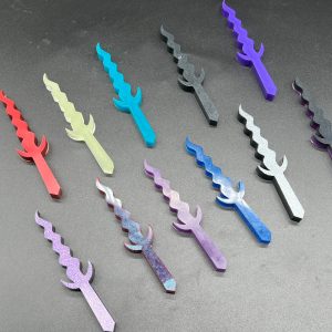 An array of Kris style daggers. Top row, left to right: Red, glow in the dark, turquoise, black, purple. Bottom row, left to right: purple sparkle, red and turquoise, purple, blue, silver sparkle, black and purple