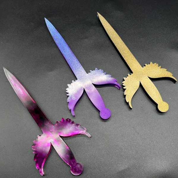 Three Poignard resin daggers, left to right: translucent purple, holographic purple, and gold and black