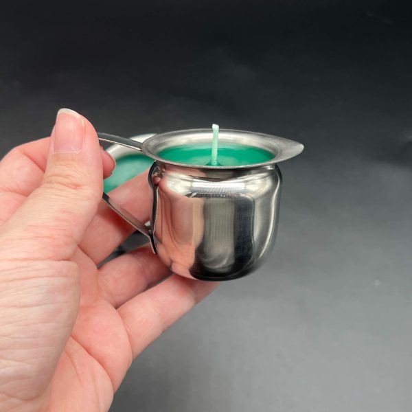 Kayla holding the 3 ounce green paraffin candle by the handle in a side view to show the spout