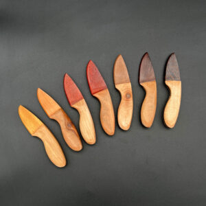 Seven skinner wooden knives made with different wood blades. From left to right: Iroco, Cherry, Paduak, Bloodwood, Black Walnut, Rosewood, and Wenge