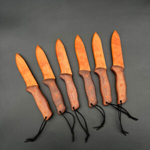 Six spearpoint wooden knives in a row. Each one has a cherry blade, a red-brown wood and a black walnut handle, a dark brown wood. The blade is about 4.5 inches long and the handle is about 4 inches long